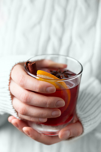 A girl in a soft knitted sweater holds a cup of mulled wine with both hands