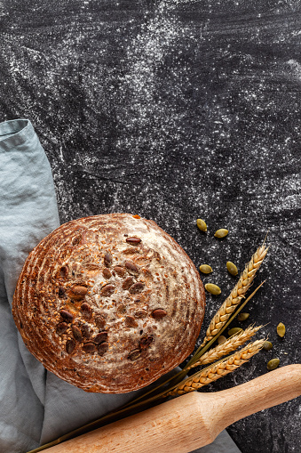 Loaf of homemade, fresh bread with sunflower seeds and linseed on wooden background