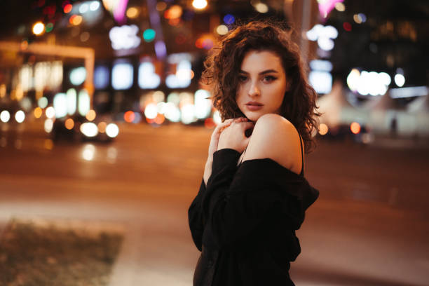 istock Girl during the night posing for the camera with artificial lights illuminating her with shallow depth of field. Girl flirting with camera during the night with blank facial expression. 1275205632