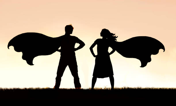 Silhouette of SuperHero Man and Woman Couple in Capes Standing Strong A silhouette of a superhero man and woman couple in capes standing strong and powerful against a sunset sky background. superhero photos stock pictures, royalty-free photos & images