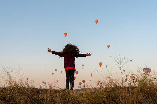 Cute little girl jumping on the hill in Cappadocia, Hot air balloons seen on the sky