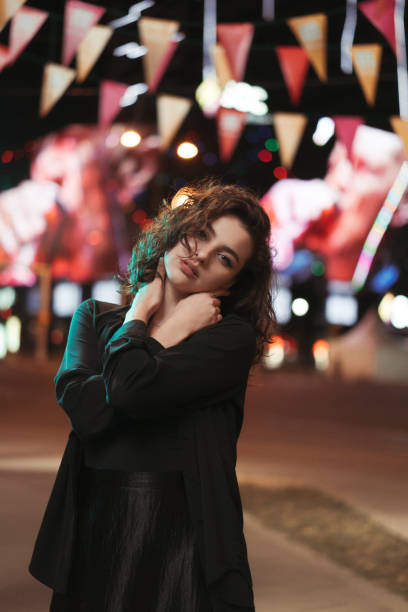 istock Girl during the night posing for the camera with artificial lights illuminating her with shallow depth of field. Girl flirting with camera during the night with blank facial expression. 1275207196