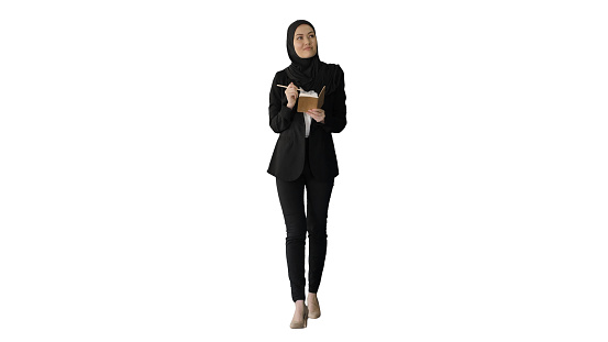 Wide shot. Front view. Muslim Businesswoman thinking and writing ideas in her notepad while walking on white background. Professional shot in 4K resolution. 043. You can use it e.g. in your medical, commercial video, business, presentation, broadcast