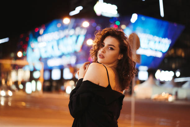 istock Girl during the night posing for the camera with artificial lights illuminating her with shallow depth of field. Girl flirting with camera during the night with blank facial expression. 1275242936