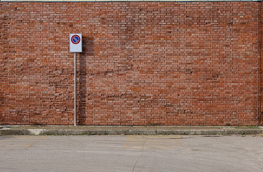 Grunge brick wall with a no stop road sign. A sidewalk and asphalt street in front. Background for copy space