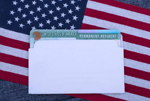 Permanent resident card (Green card) in white envelope on American flag and blue fabric surface. Free copy space for text.
