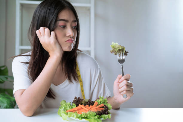 malheureuse fille asiatique, elle s’ennuyait quand elle a dû manger des légumes. - dieting food rejection women photos et images de collection