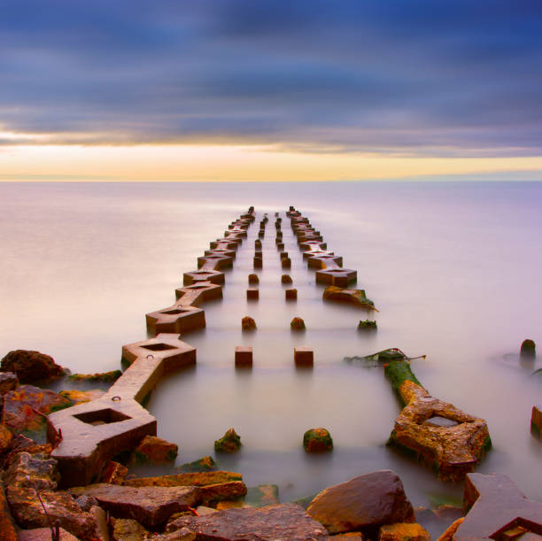 Mysterious ruins of pier structure built by ancient civilization, framed in misty water surface, long exposure.