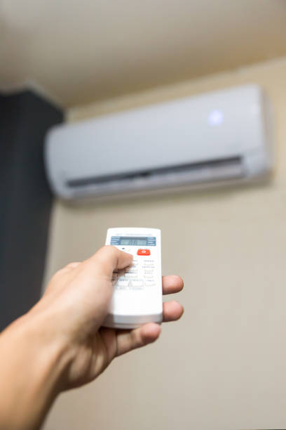 istock man's hand holding air conditioning unit remote control aimed at the AC unit 1275291242