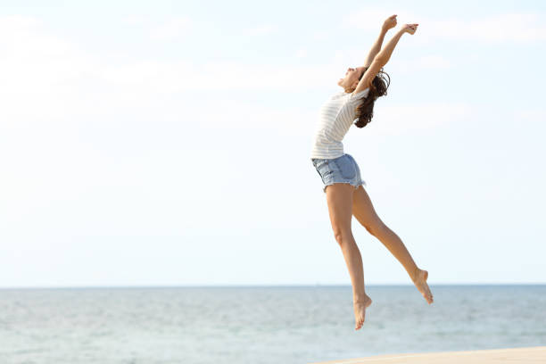 возбужденная женщина с длинными ногами прыгает на пляж - full hair стоковые фото и изображения