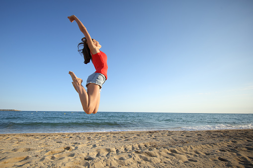 Happy teen in red jumping on the beach a sunny day