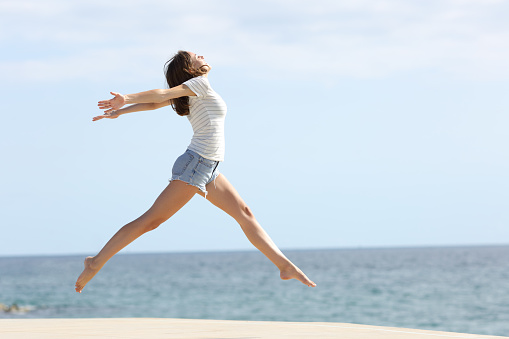Happy woman enjoying while jumping during summer vacation on the beach. Copy space.