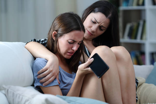 Sad teen with phone being comforted by her sister Sad teen with phone being comforted by her sister cyberbullying stock pictures, royalty-free photos & images