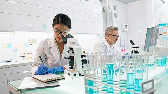 Modern laboratory interior. Neurological Research Laboratory. Asian ethnicity woman using microscope, team working on medical samples in background