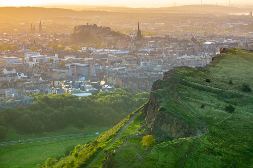 Edinburgh Castle In The Gentle Orange Glow Of A Summer Evening, With Salisbury Crags In The Foreground