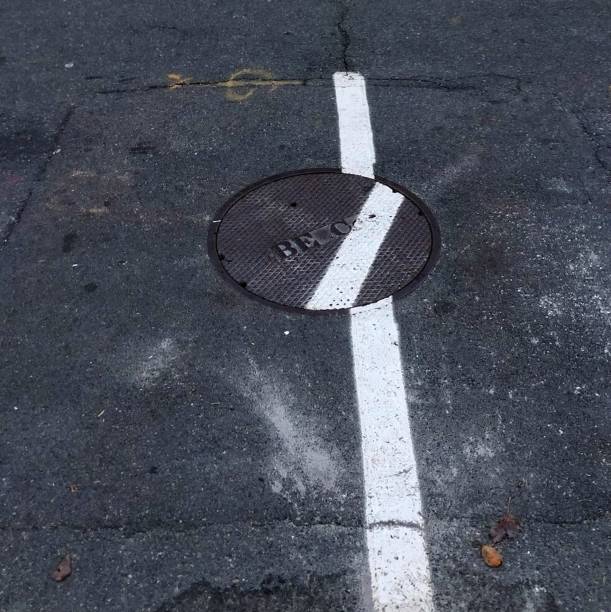 istock White Line Painted on Road w/Crooked Sewer Cover 1275344876