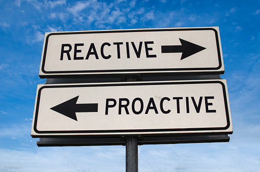 Reactive vs proactive. White two street signs with arrow on metal pole with word. Directional road. Crossroads Road Sign, Two Arrow. Blue sky background. Two way road sign with text.