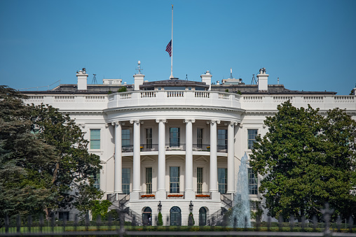 The White House, Home of the President of the United States of America in Washington, DC USA on Blue sky background. Half Staff Flag Status.