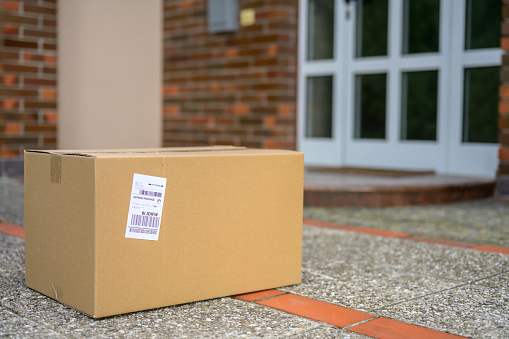 Close-up of cardboard package laying on floor in front of a house during coronavirus pandemic.