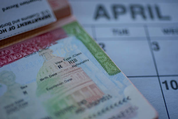 H1B visa (for specialty workers) stamp in passport, blurred april calendar on background. H1B visa program deadline concept. Close up view. stock photo