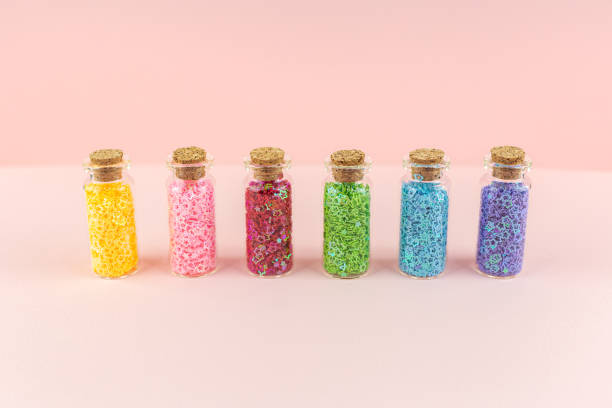 istock Small glass bottles with corks with multicolored shiny sequins asterisks stand in a row on a pink background. 1275427470