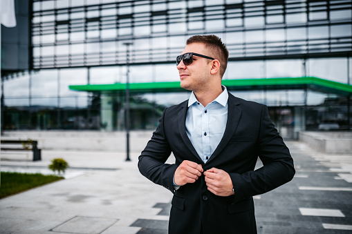 Portrait of young handsome businessman standing in front of business building.
