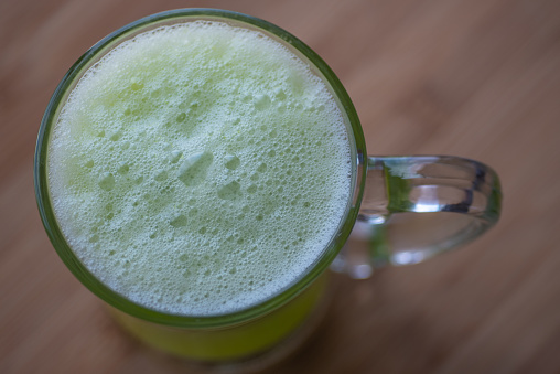 Top view of Matcha chai tea latte foam in glass mug (cup) on wooden surface.