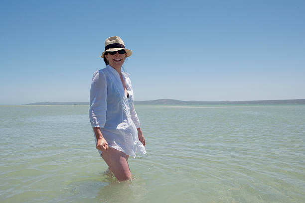 vecchia donna camminare nell'acqua - women wading sun hat summer foto e immagini stock