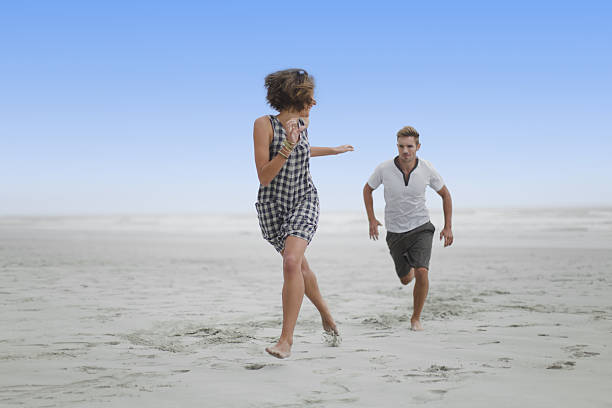 coppia, inseguendosi l'altro sulla spiaggia - chasing women men couple foto e immagini stock