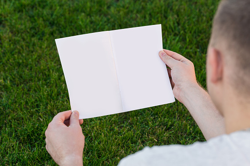 mens hands open a blank catalog, magazines, book mockup on the background of a green lawn