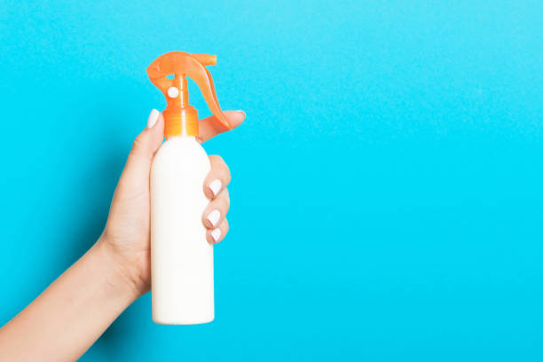 istock Female hand holding cosmetics spray at blue background with empty space for your design 1275494471