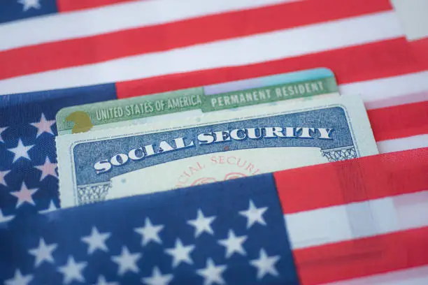 Photo of USA Permanent Resident (Green card) and Social security number (SSN) covered on American flag.