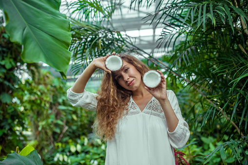 Greenhouse. Woman in white dress with coconut in her hands smiling