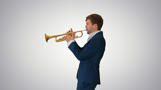 Medium shot. Side view. Young man in suit playing a trumpet on gradient background. Professional shot in 4K resolution. 047. You can use it e.g. in your medical, commercial video, business, presentation, broadcast