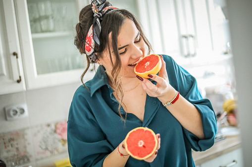 Portrait of girl holding red grapefruit - Young woman is holding a grapefruit while sitting in her kitchen and enjoying a non-working day