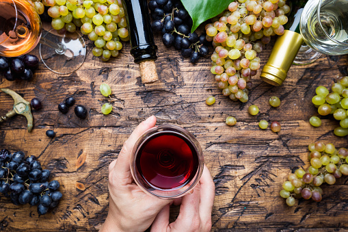 Glasses with white, red and pink wine and ripe grapes on wooden background, top view. womans hand with wine glass