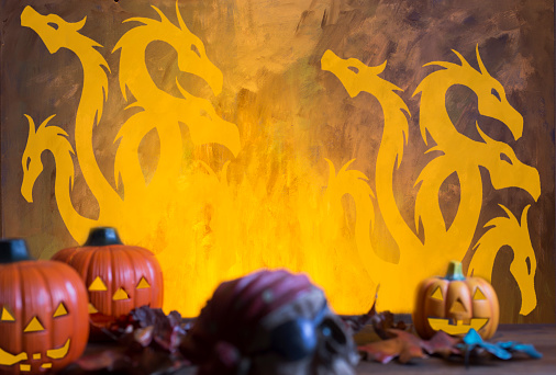 Bright orange background appears as to be an inferno with Halloween decorations in foreground and in the blazes in background.
Hydra in background.