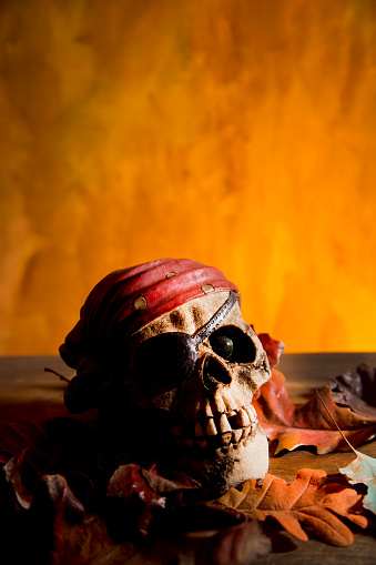 Bright orange background appears as to be an inferno with Halloween decorations in foreground.  Pirate head in foreground.
