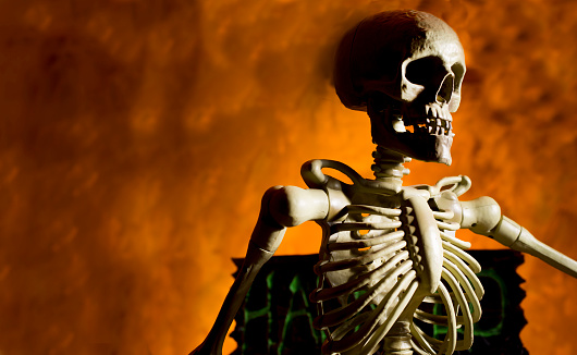 Bright orange background appears as to be an inferno with Halloween decorations in foreground.  Skull and torso in foreground.