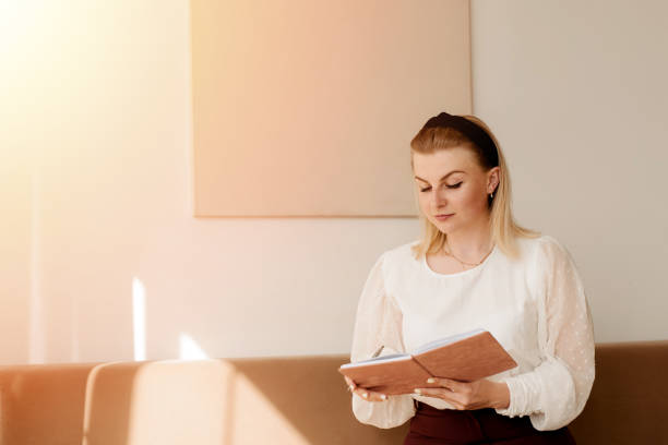 istock Young beautiful woman sitting on a sofa with a diary and making a day plan 1275588798