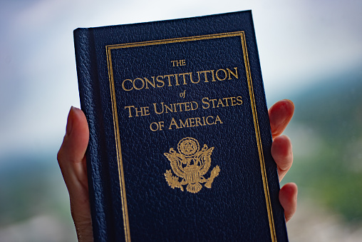 The Constitution of The United States of America book in hand on blurred background.