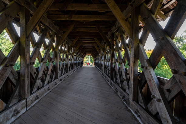Lucerne, Switzerland - October 16, 2012: Lucerne Switzerland Chapel bridge interior with paintings hanging from the ceiling. Some people are walking, crossing the bridge in the distance. Jesuit church visible beyond the bridge.