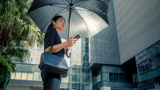 In the City After work, asian women holding umbrellas Use a mobile phone to call a taxi During the rain.