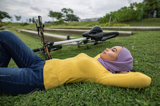 Asian women lying down at grass with bicycle. She is closing her eyes and enjoy the weather.