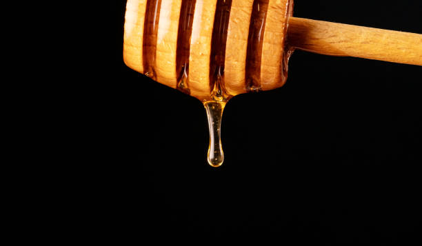 istock Honey dripping from wooden honey dipper on black background. 1275663371