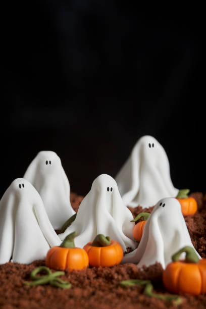 istock Sugar paste scene of halloween, group of ghosts in a pumpkin patch, chocolate cake ground, dark textured background, copy space 1275676937