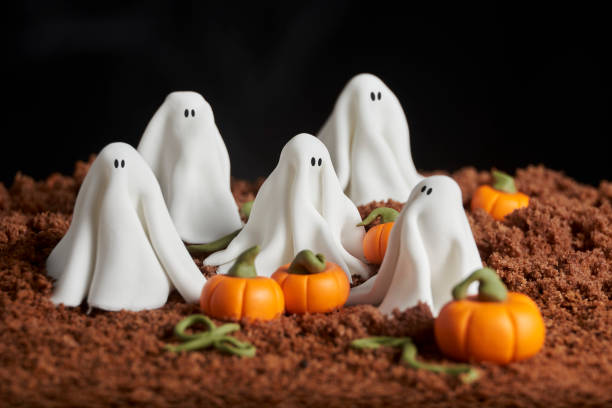 istock Sugar paste scene of halloween, group of ghosts in a pumpkin patch, chocolate cake ground, dark textured background, copy space 1275676955