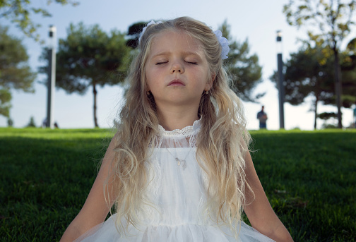 little girl in a white dress on a green lawn meditation