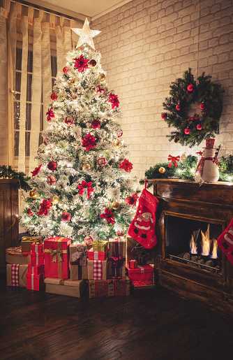 Beautifully decorated living room with fireplace and gifts under big Christmas tree on Christmas Eve. Luxury home with holidays decorations, burning fire and lots of presents under the Christmas tree