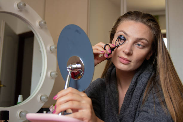 istock Young woman using eyelash curler while relaxing at home 1275687042